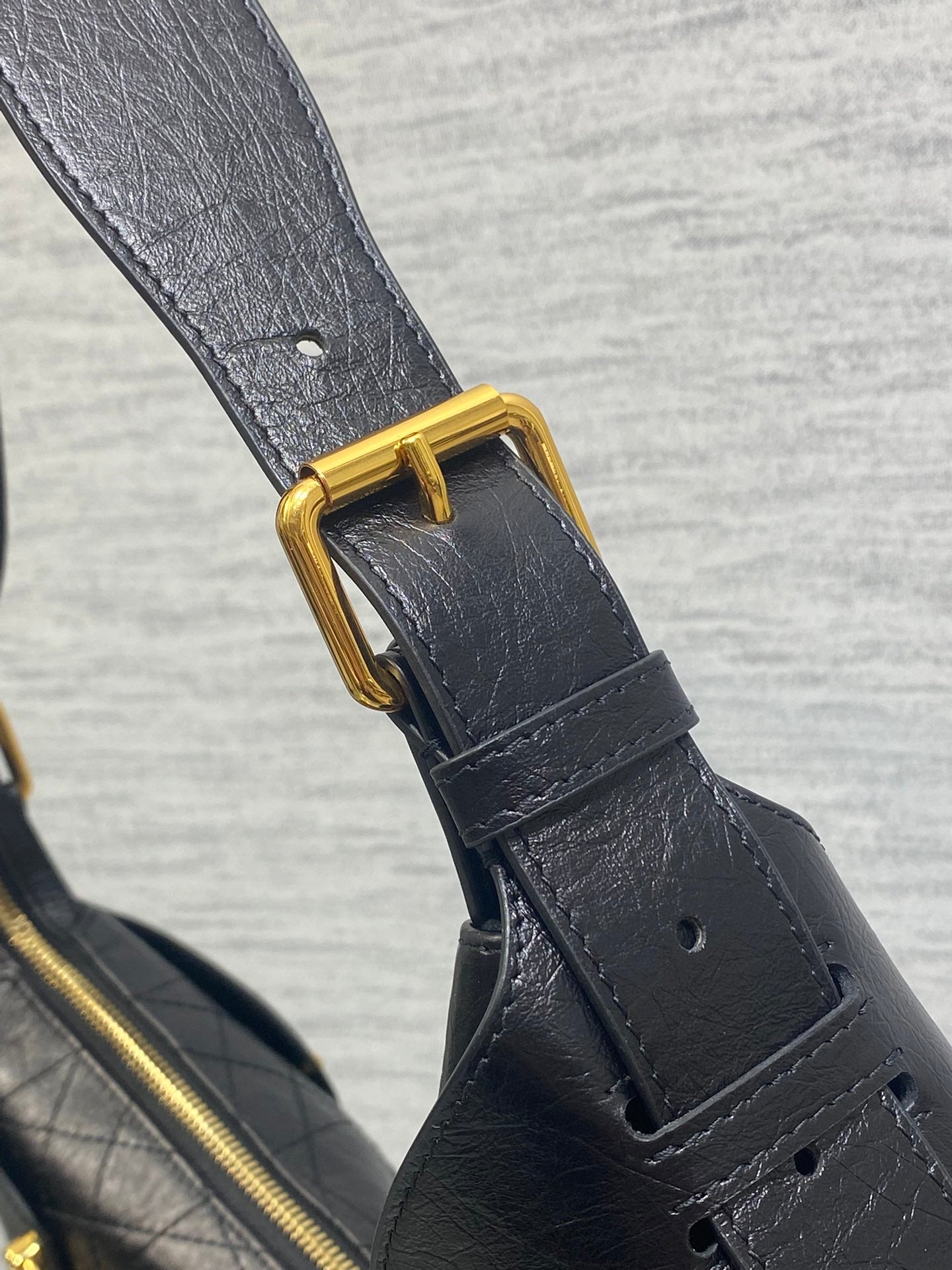 Black leather strap with gold buckle hardware and stitched fastening tab