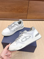 White Dior low-top sneakers with gray laces and side logo, held above navy box