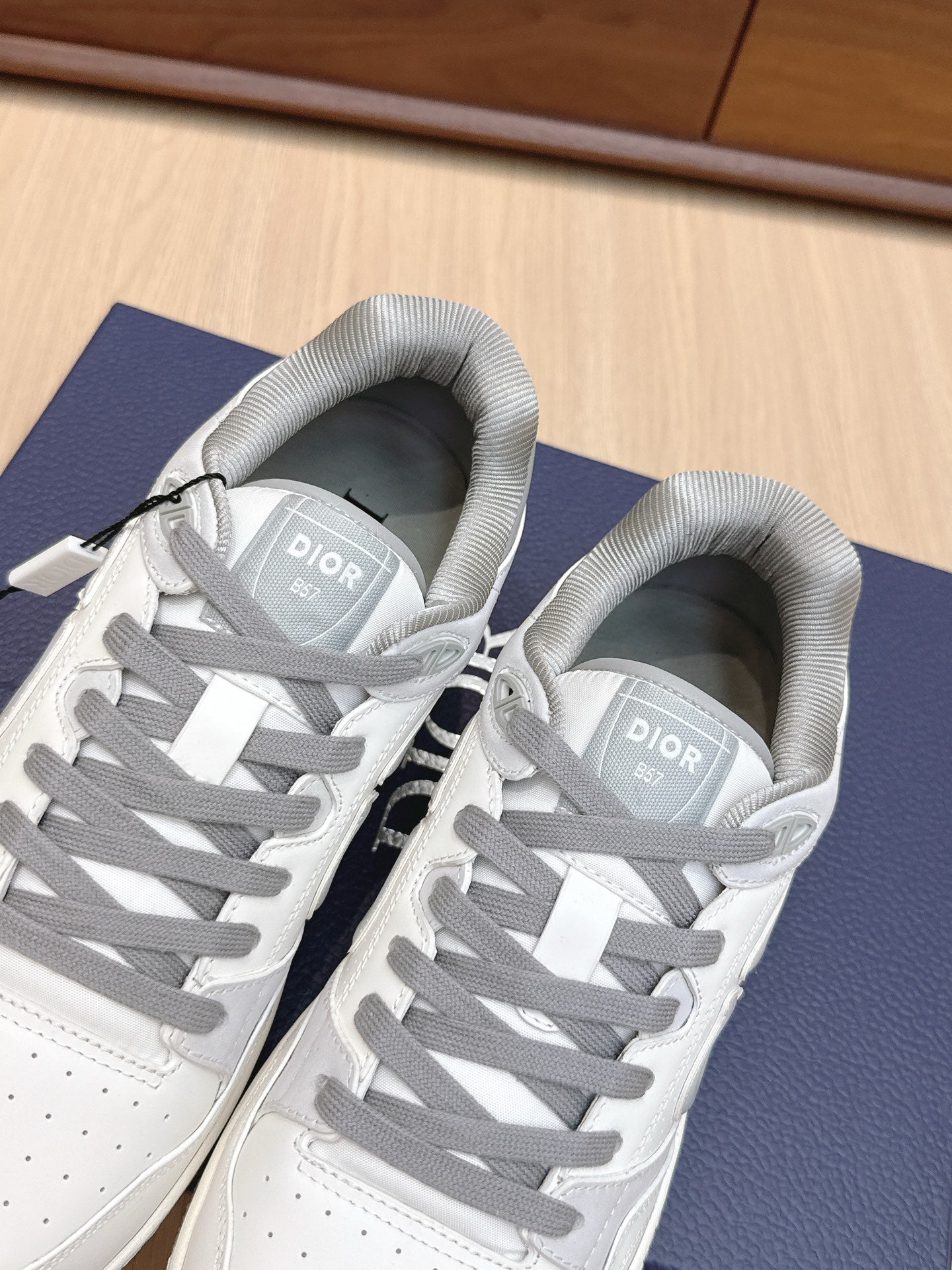 White Dior sneakers with gray laces and tongue labels, side view pair on box