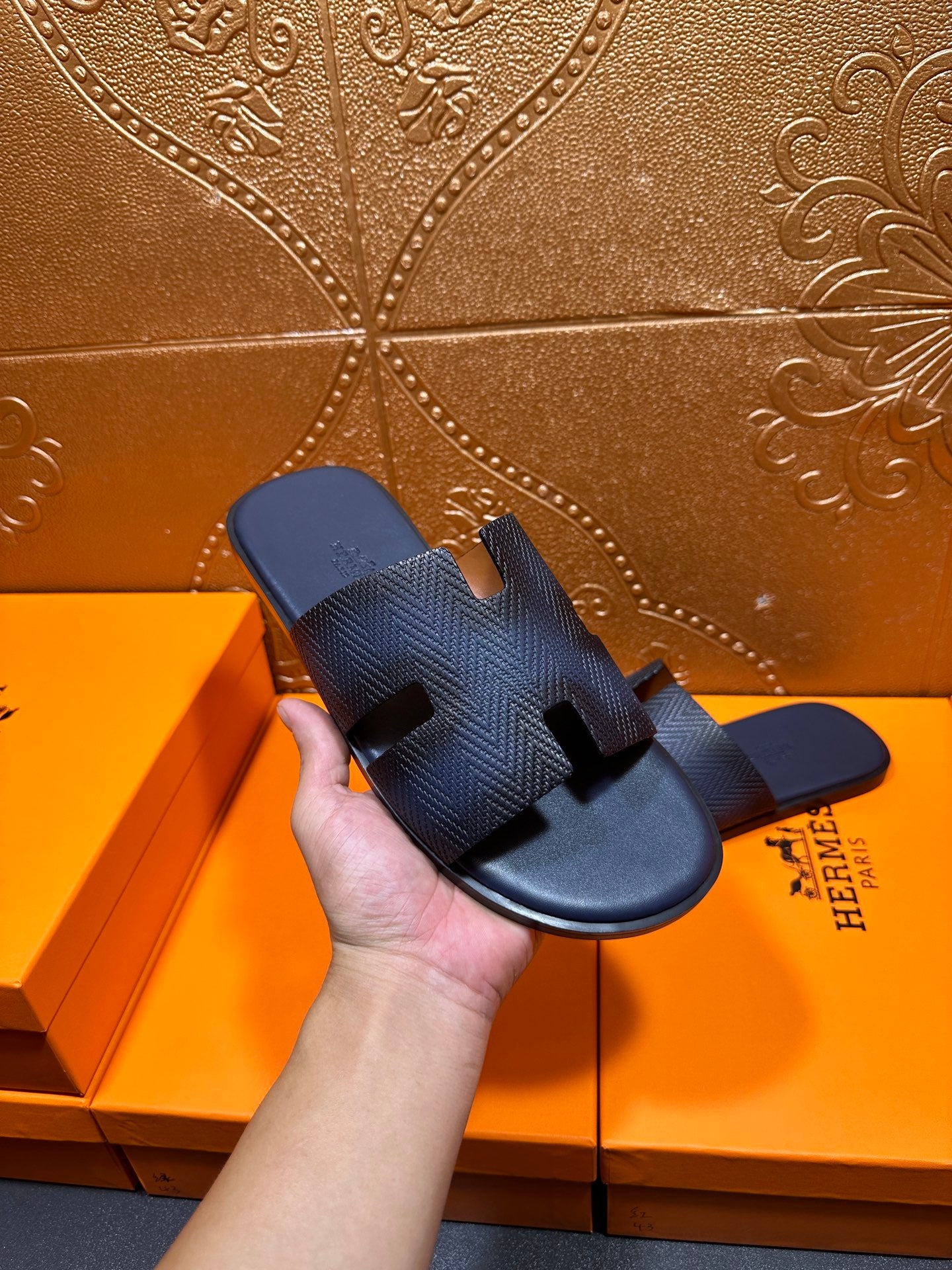 Hand holding dark blue textured leather slide sandals with open toe and H strap