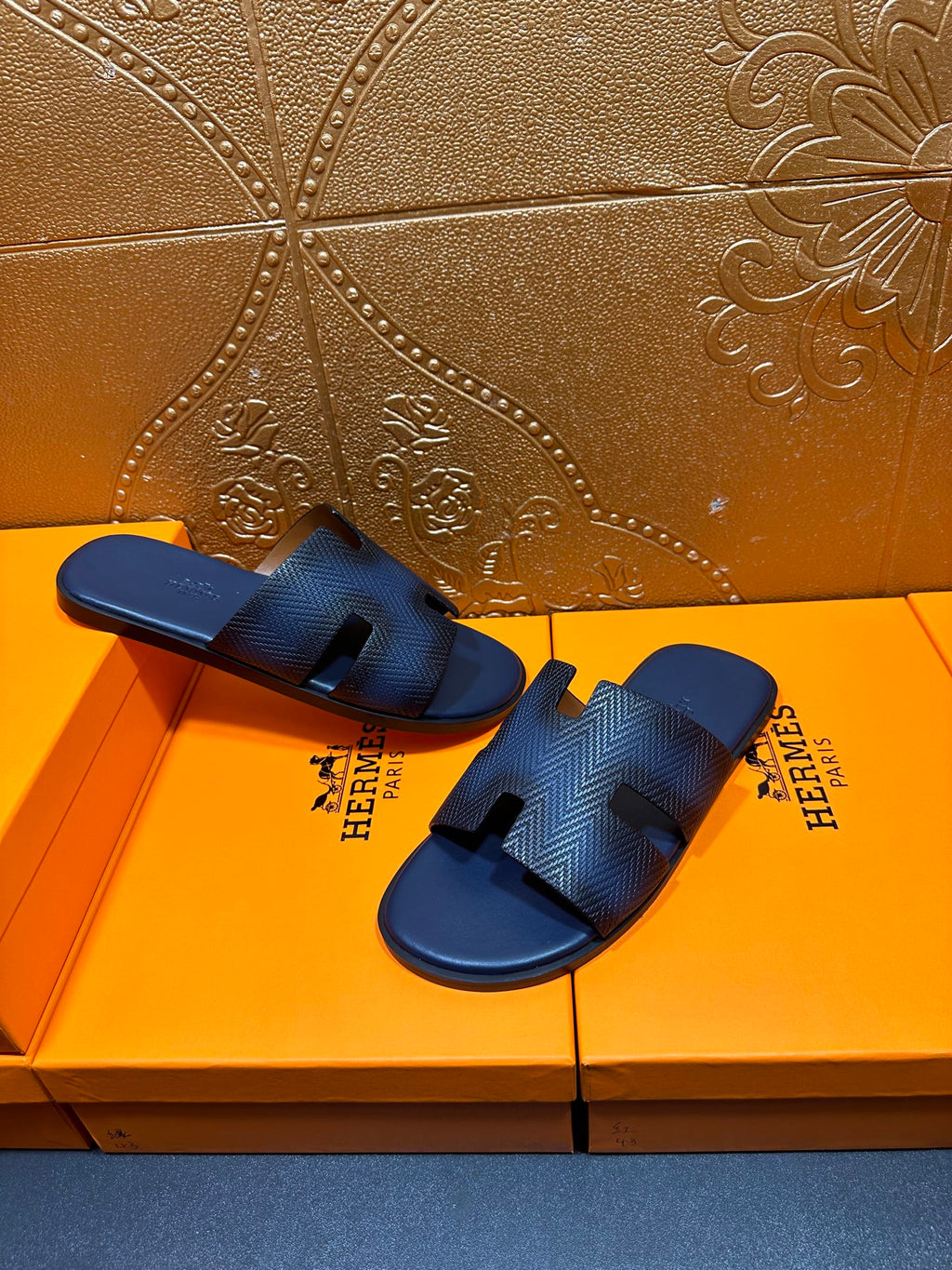 Pair of dark blue textured leather slide sandals with open toe and H-shaped cutouts