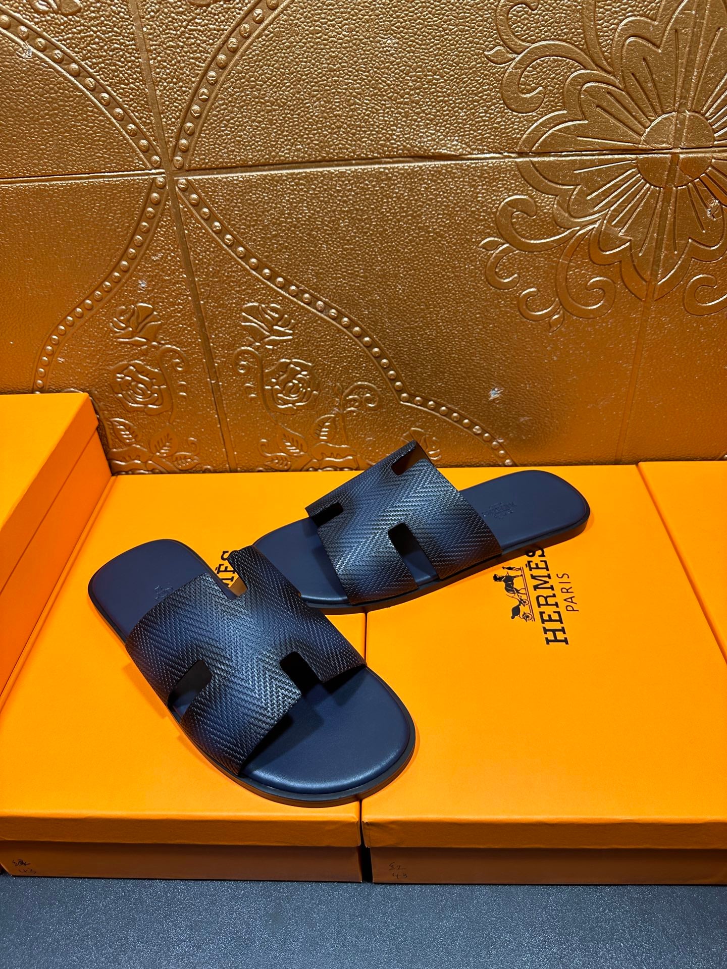 Pair of dark blue textured leather slide sandals with open toe and H cutouts
