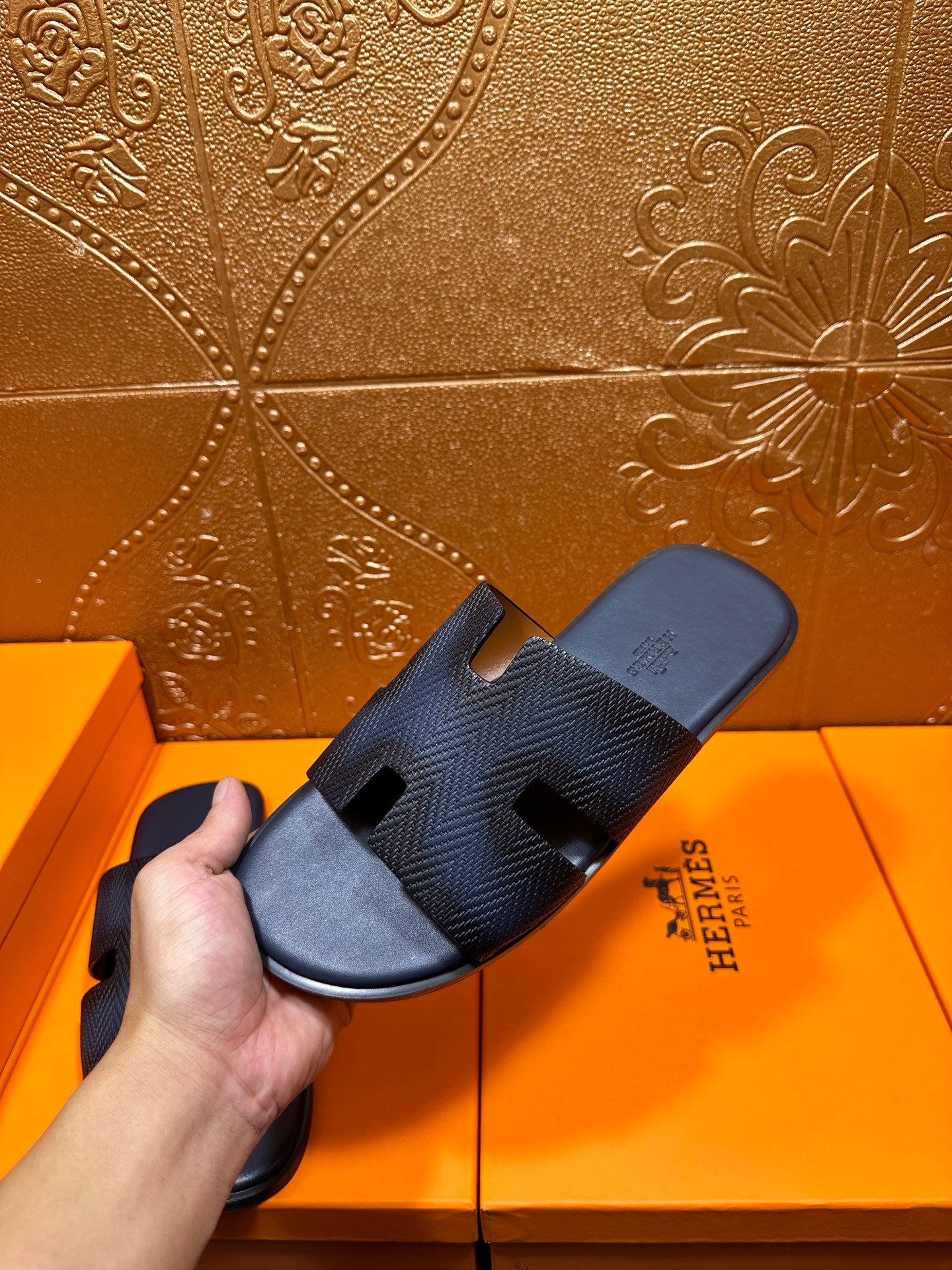 Hand holding dark blue textured slide sandals with open toe and H-style straps