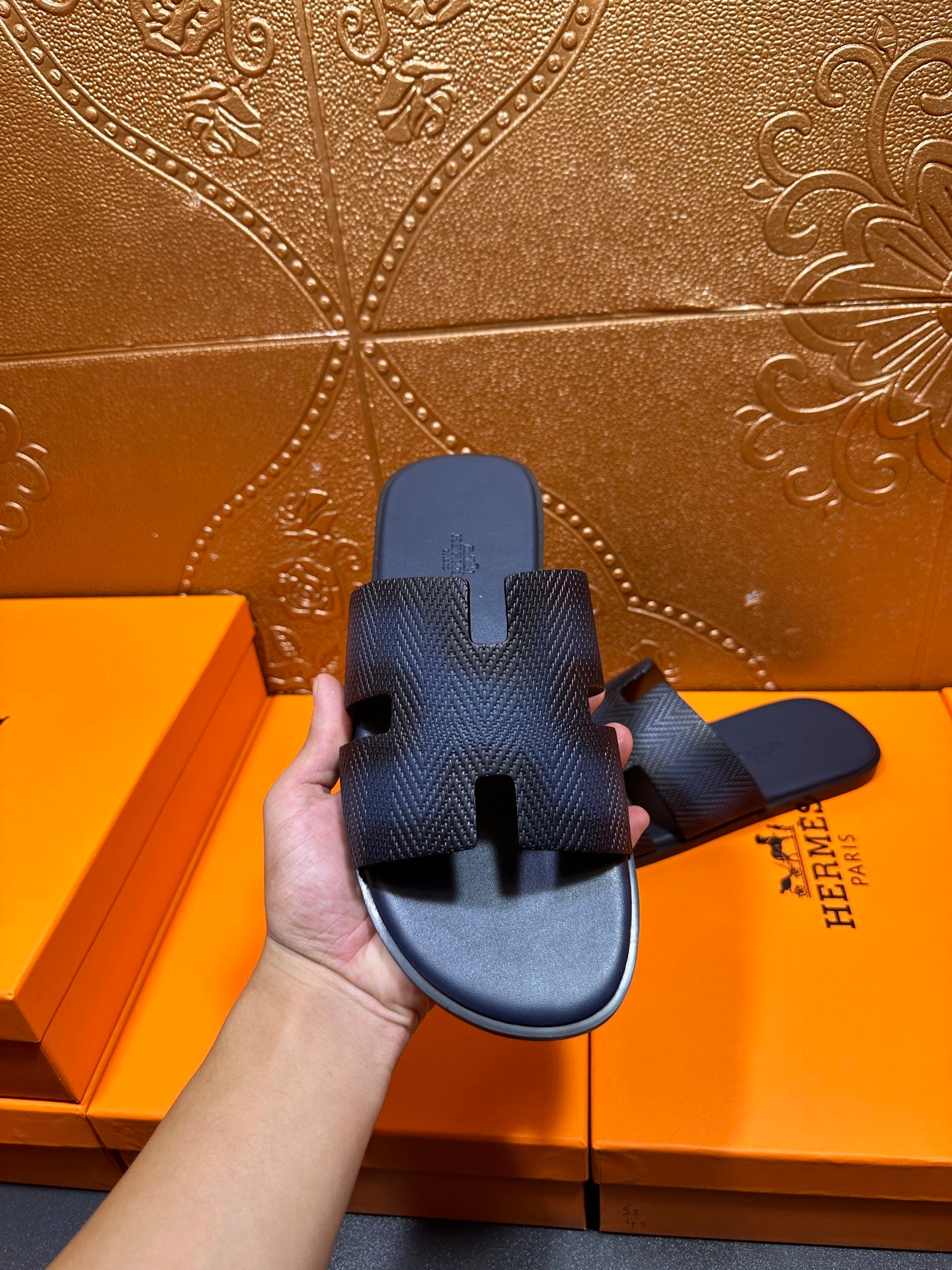 Dark blue textured slide sandals shown from the back with open toe and H cutouts
