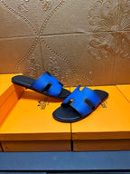 Hermes blue slide sandals with black footbed and H cutout strap, lifted view