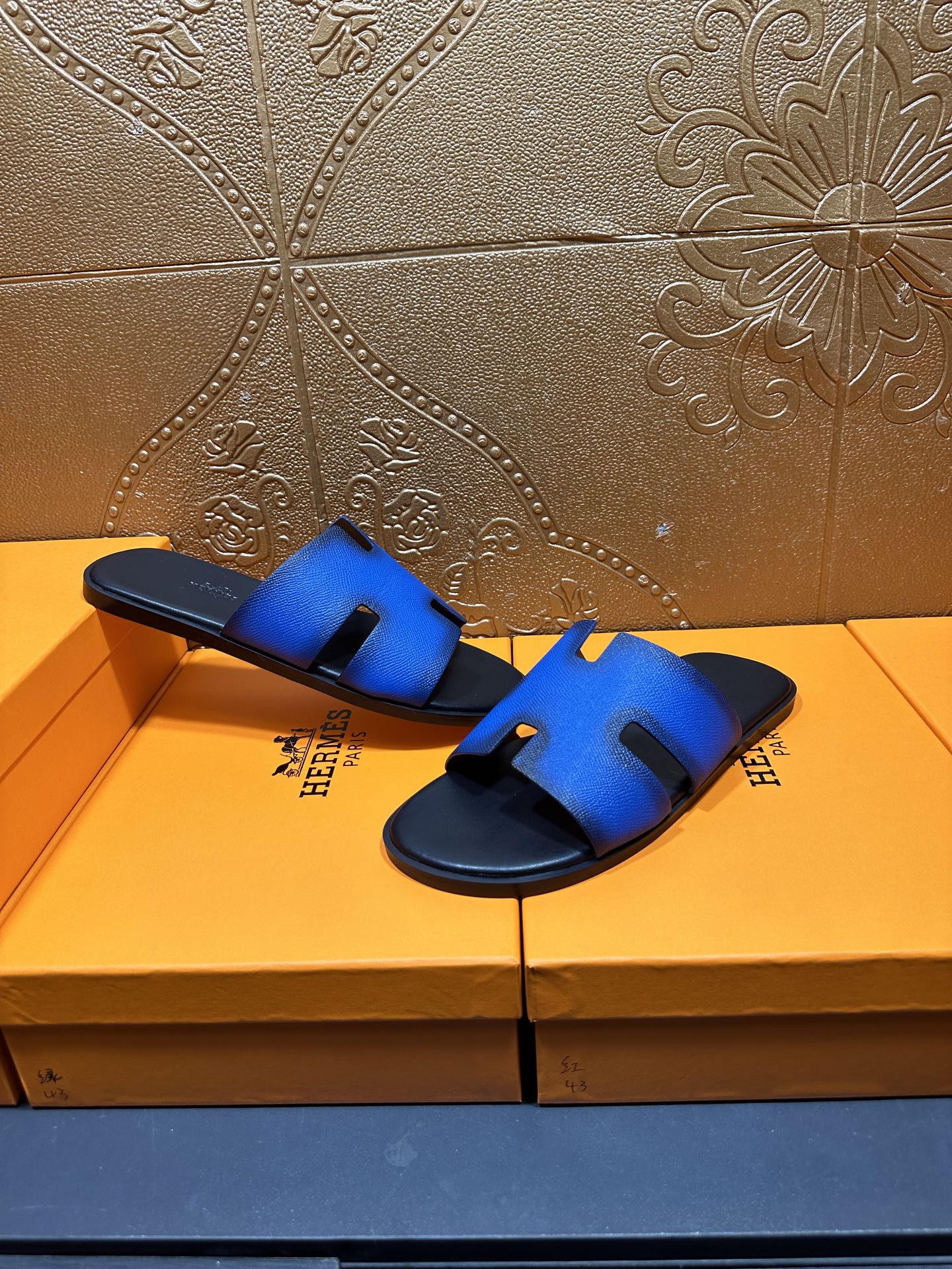 Hermes blue slide sandals with black footbed and H cutout strap, lifted view