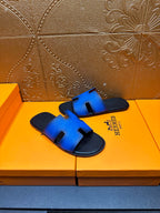 Hermes blue slide sandals with black strap trim and H cutout, angled view