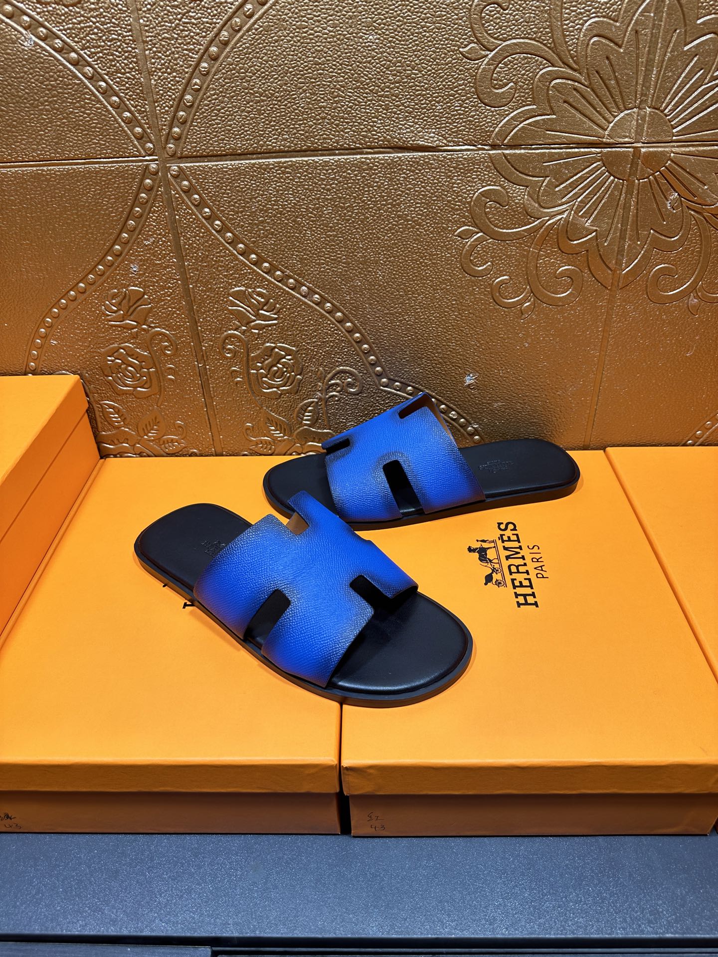 Hermes blue slide sandals with black strap trim and H cutout, angled view
