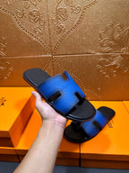 Hermes blue slide sandal held in hand, black footbed and H cutout strap