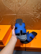 Hermes blue slide sandals with black footbed and H cutout, hand-held angle