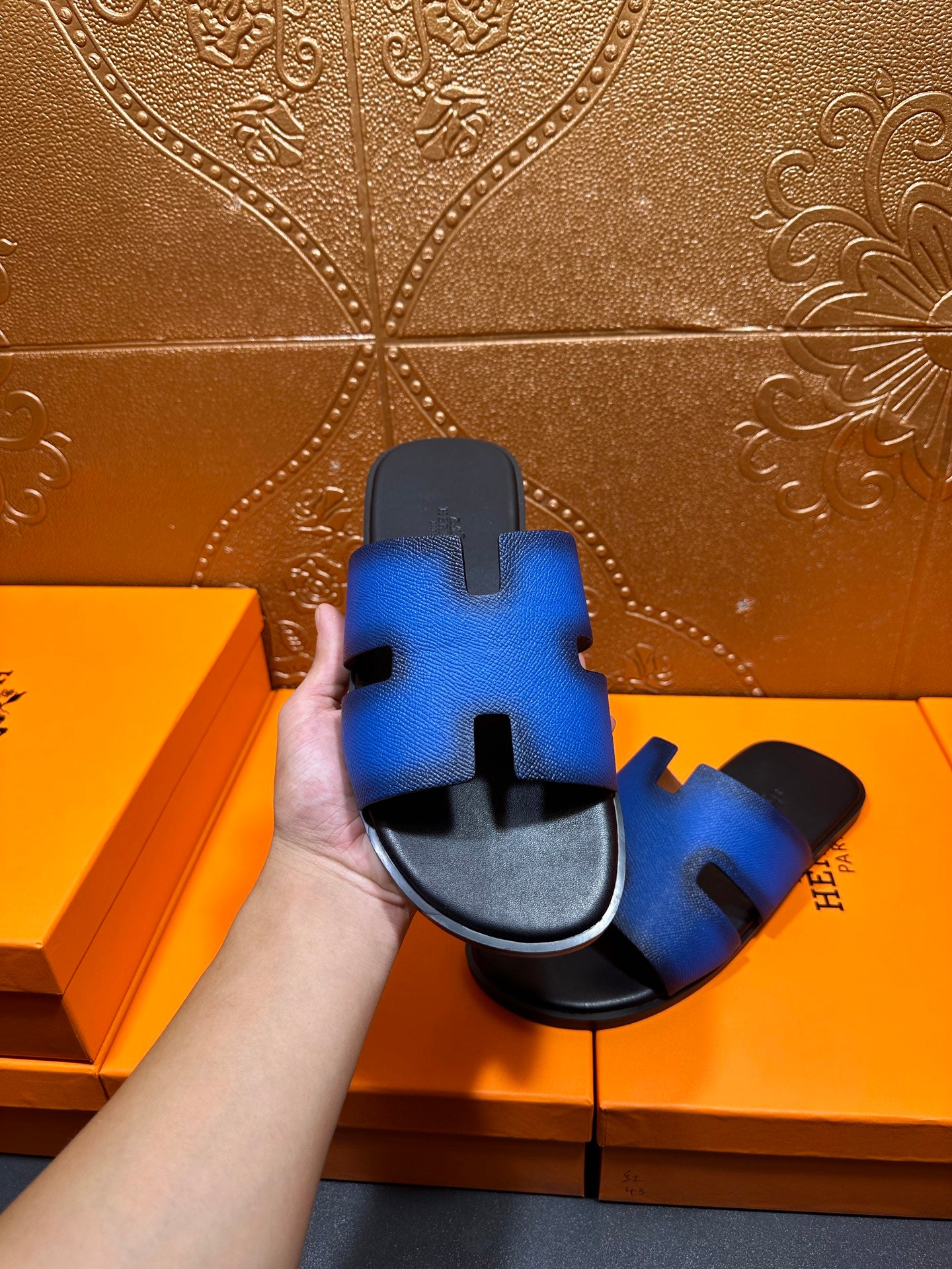 Hermes blue slide sandals with black footbed and H cutout, hand-held angle