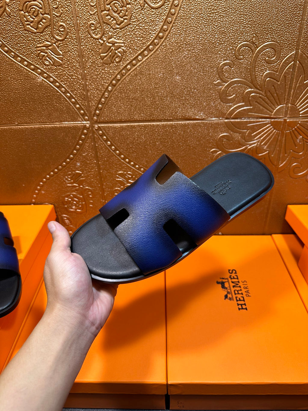 Blue leather slide sandal held up, showing cushioned footbed and slip-on sole