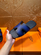Blue leather slide sandal held up, showing cushioned footbed and slip-on sole