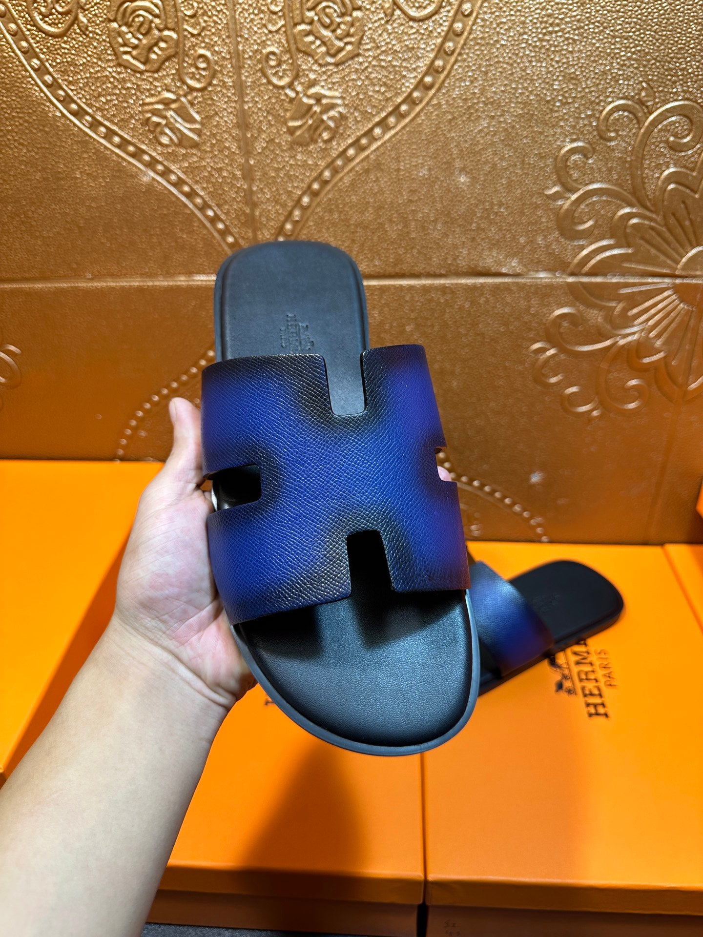 Blue leather slide sandal held in hand, showing toe opening and side strap cutouts
