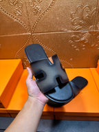 Hand holding dark blue leather slide sandals with wide strap and open toe.