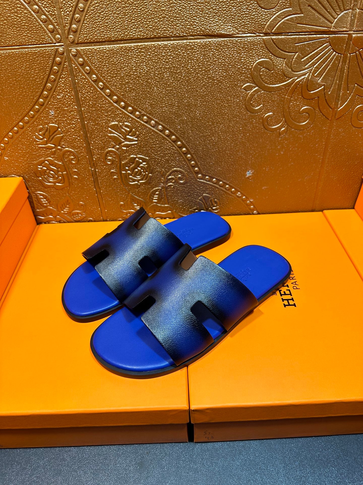 Pair of blue textured slide sandals with black cutout straps and Hermes branding on side