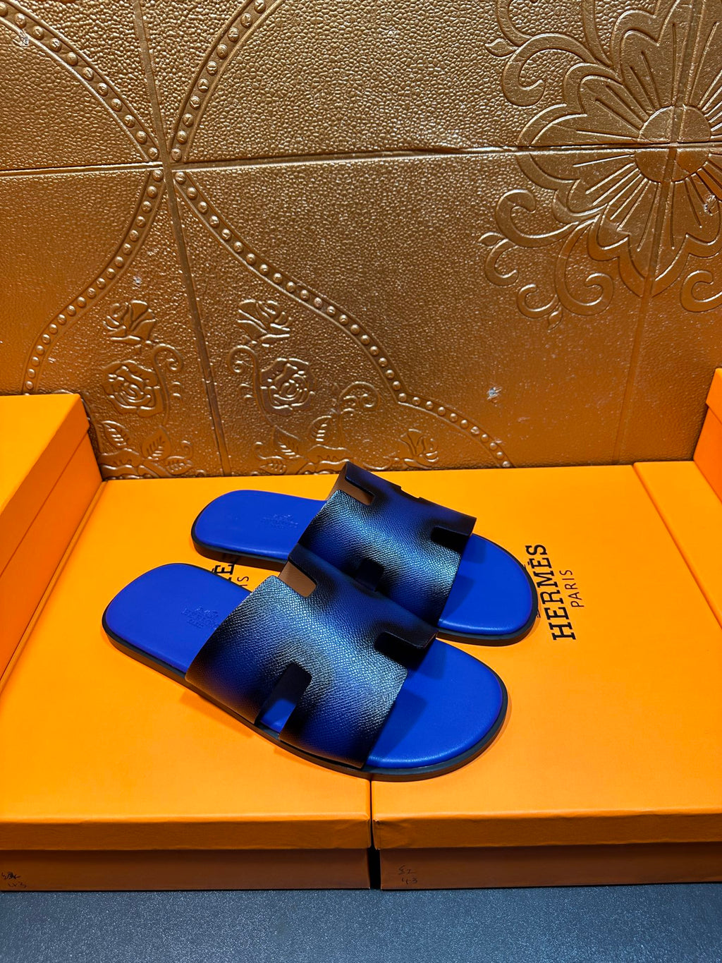 Blue textured slide sandals with black cutout bands, Hermes logo visible on strap
