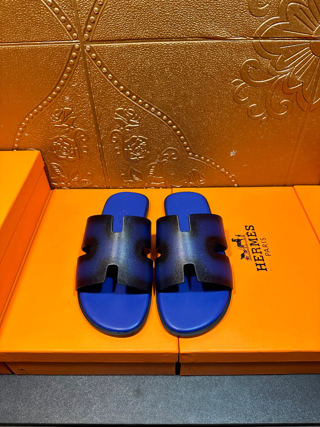 Blue textured slide sandals with black cutouts and wide strap, Hermes logo on side