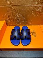 Blue textured slide sandals with black cutouts and wide strap, Hermes logo on side