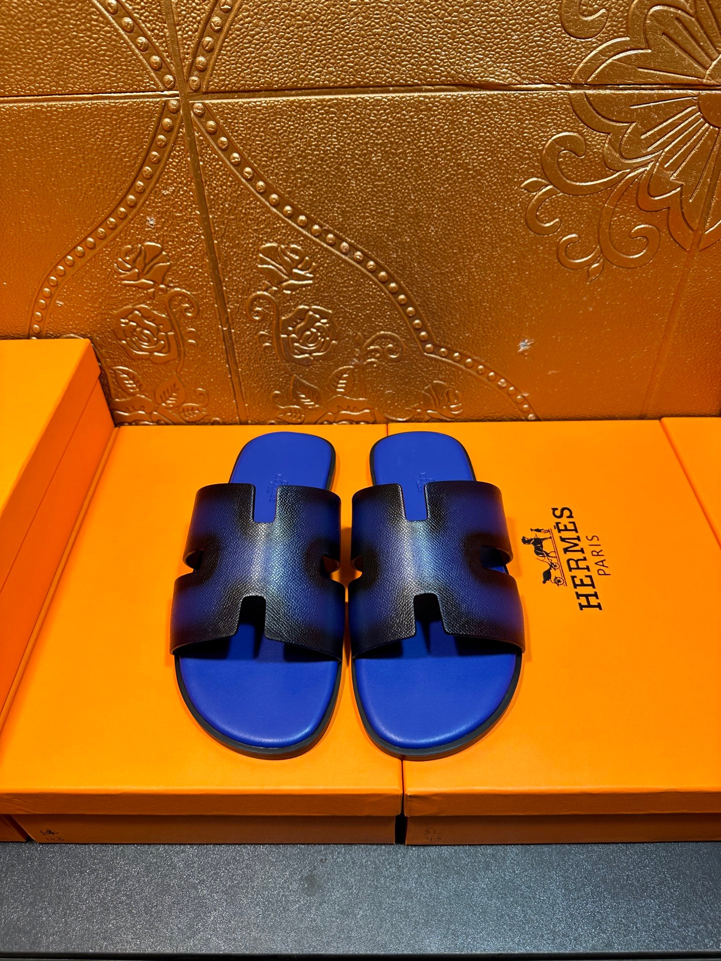 Blue textured slide sandals with black cutouts and wide strap, Hermes logo on side