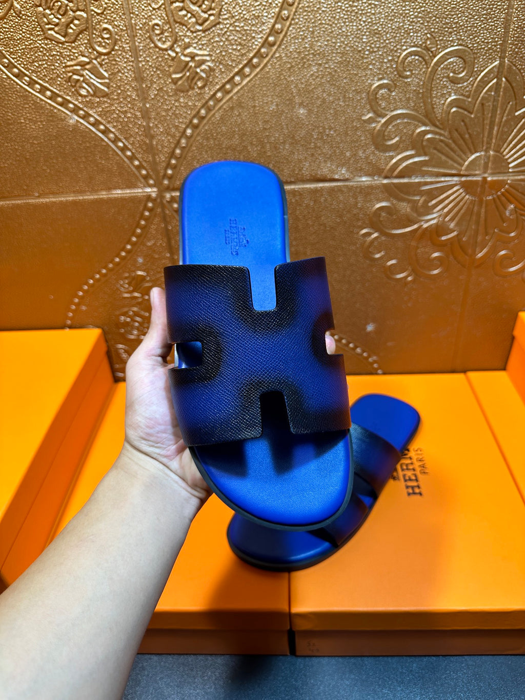 Blue textured slide sandal held up, textured footbed with Hermes logo on side