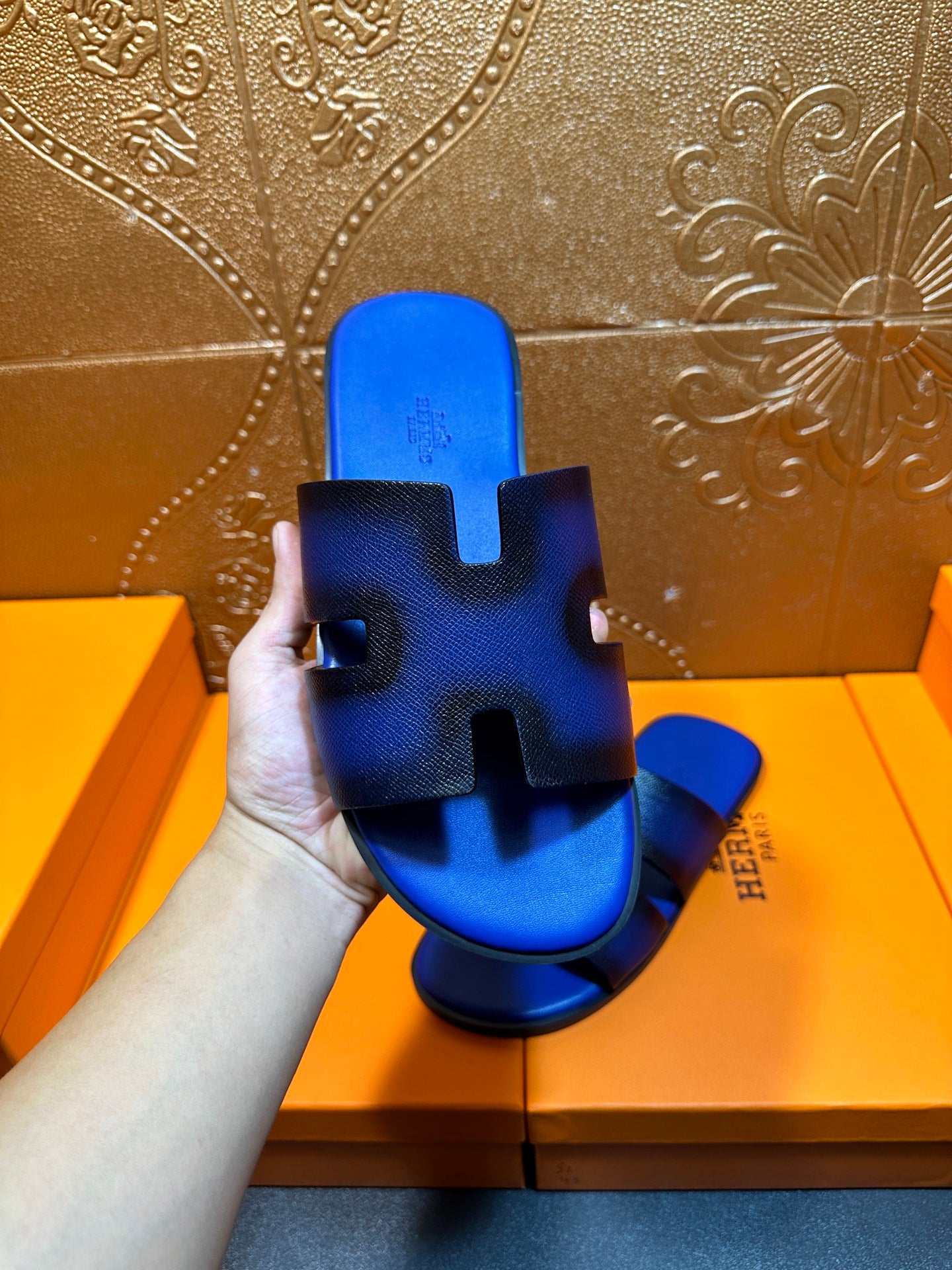 Blue textured slide sandal held up, textured footbed with Hermes logo on side