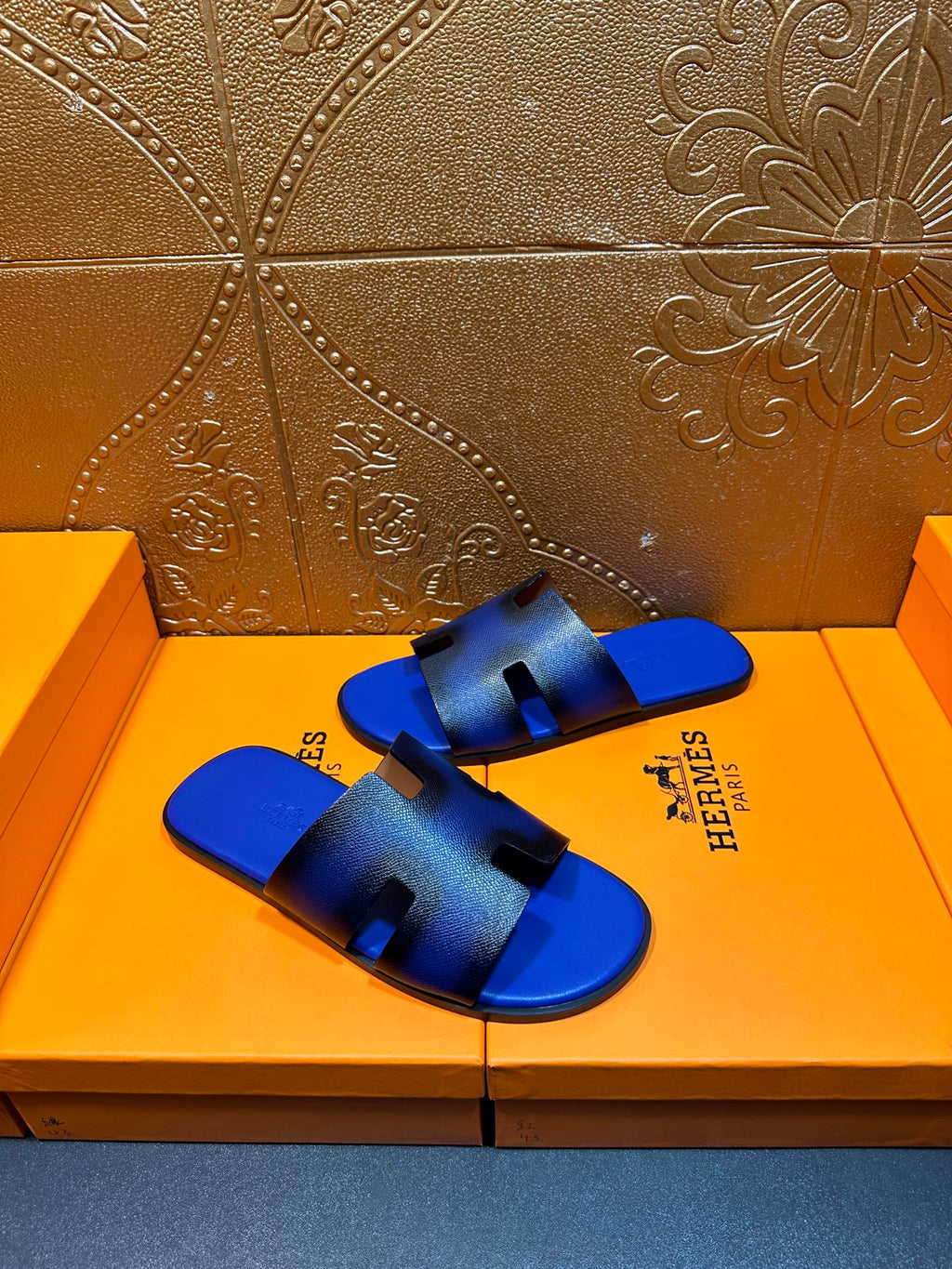 Blue textured slide sandals with black cutouts and Hermes branding on side of strap
