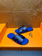 Blue textured slide sandals with black cutouts and Hermes branding on side of strap
