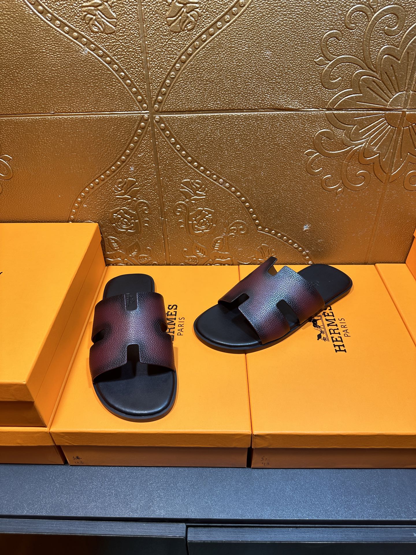 Hermes slide sandals pair on display, H cutout straps, dark textured leather