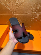 Hermes slide sandals held in hand, H cutout straps on dark textured leather