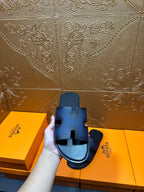 Hermes dark blue slide sandals in hand, H-shaped cutout straps and black footbed.