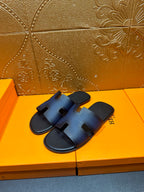 Hermes slide sandals in dark blue leather with H-shaped cutout straps.