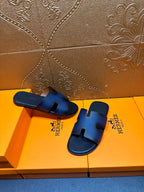 Hermes slide sandals, dark blue leather with H cutout and black molded footbed.