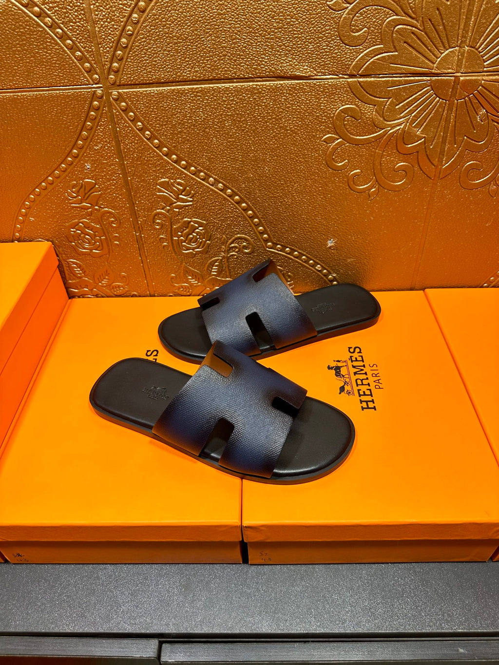 Hermes slide sandals, dark blue leather with H cutout strap and black sole.
