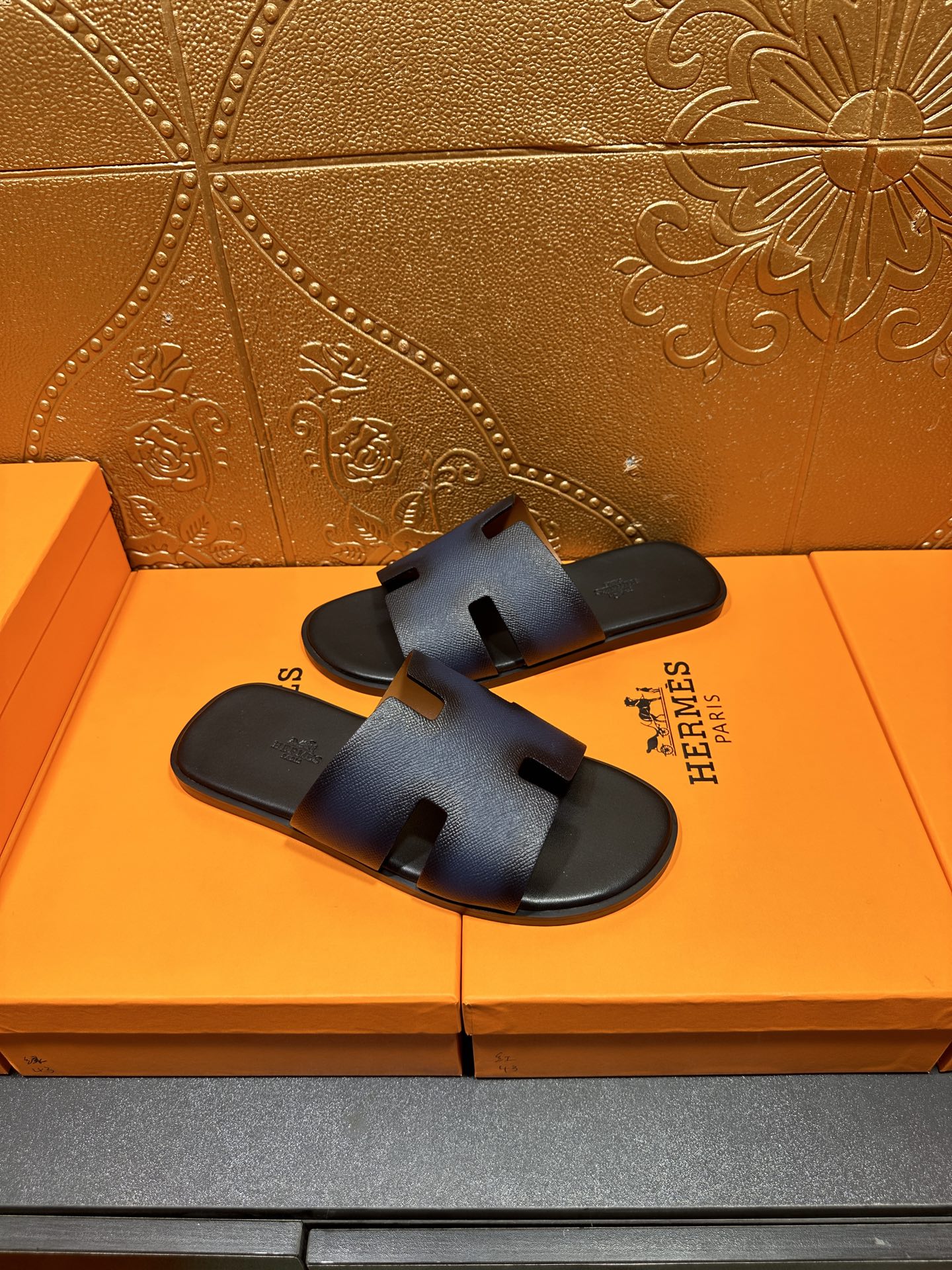 Hermes slide sandals, dark blue leather with H cutout strap and black sole.