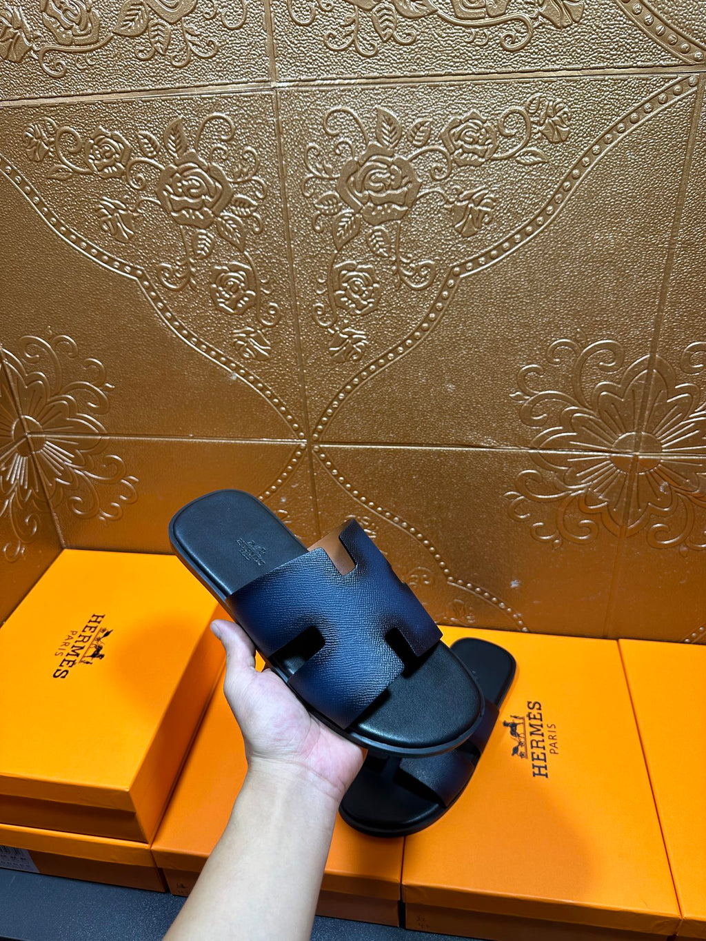 Hermes dark blue leather slide sandals held in hand, H strap and black sole.