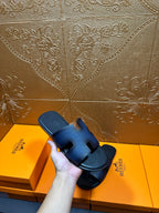 Hermes dark blue leather slide sandals held in hand, H strap and black sole.