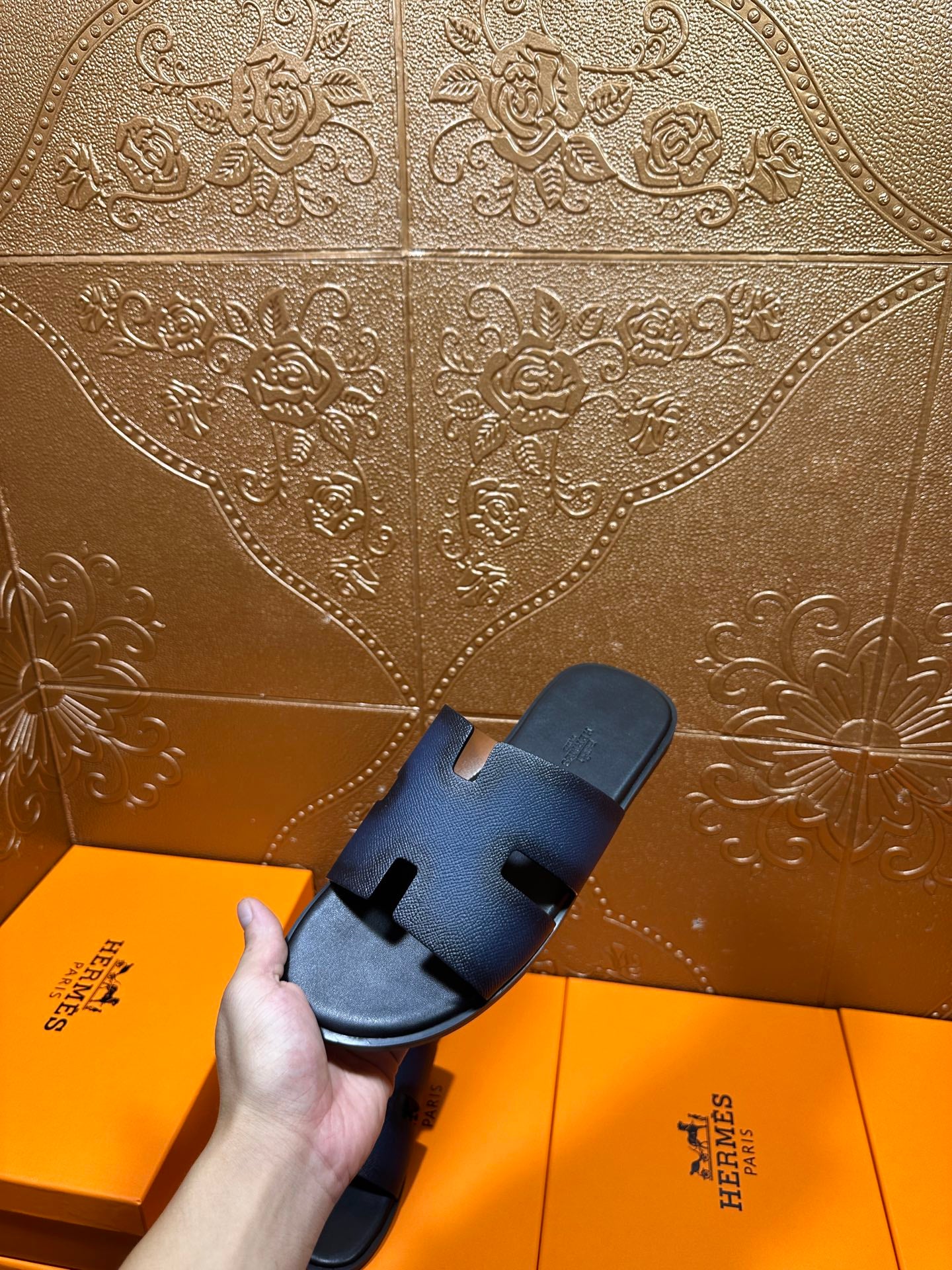 Hermes slide sandals, dark blue leather with H strap, shown held above orange box.