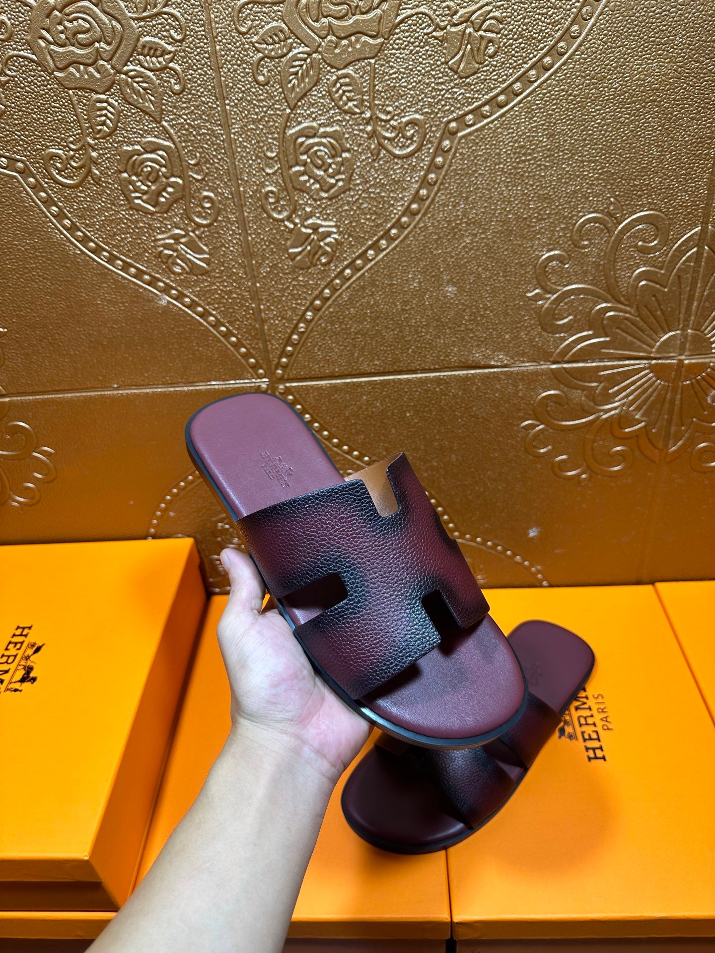 Slide sandals held in hand, dark purple leather straps with H buckle detail