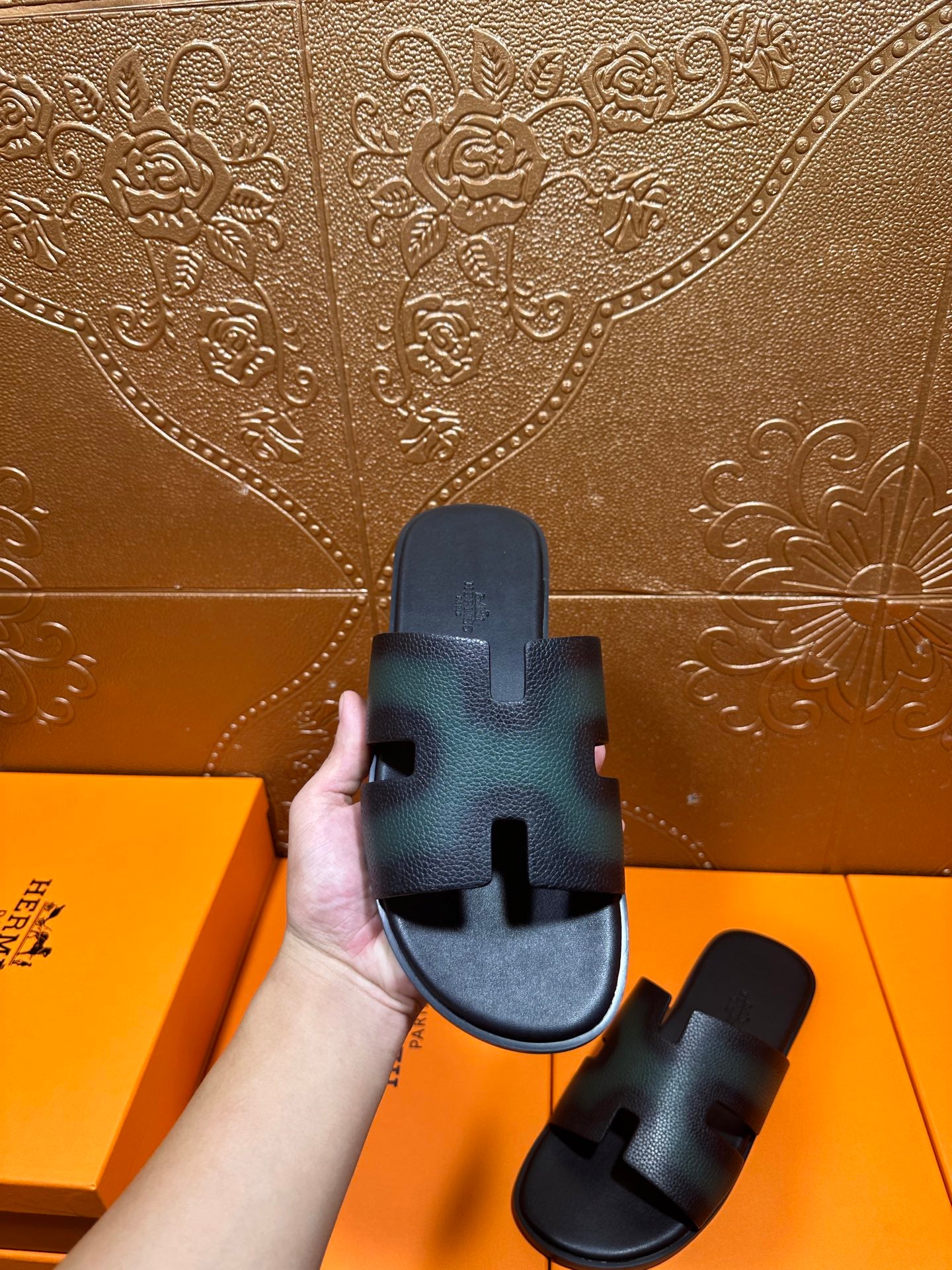Hermes sandals held up, dark teal straps with H cutout and open-toe shape