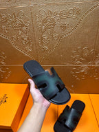 Hermes slide sandals held in hand, featuring dark teal leather straps and open toe