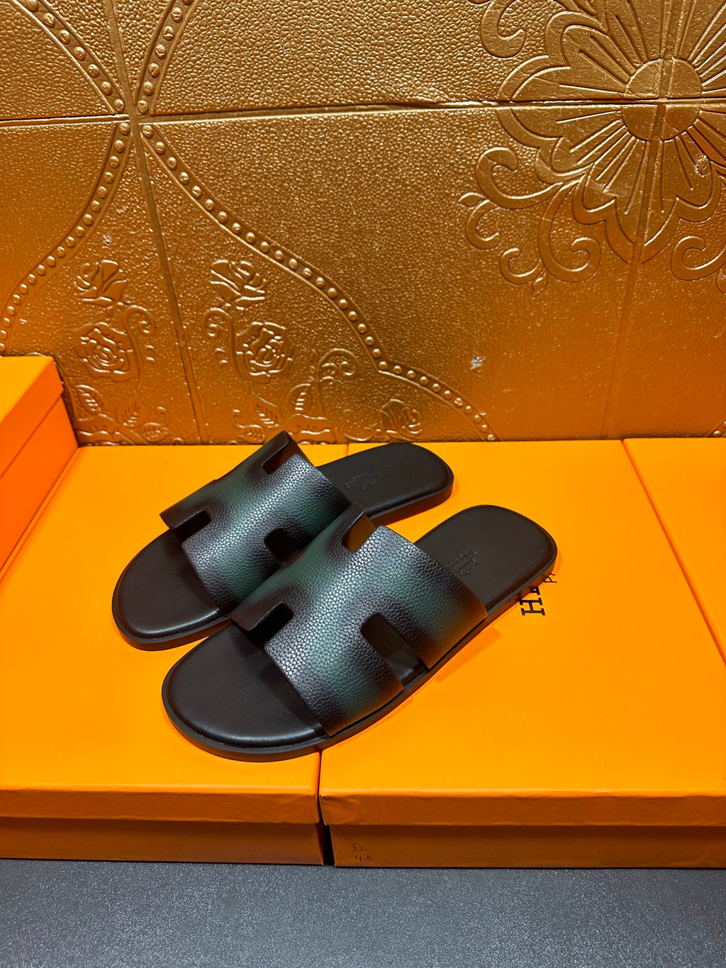 Hermes sandals on a box, showing dark teal straps with an H-style cutout