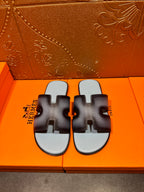 Dark navy leather slide sandals with light blue footbeds and HERMES text.