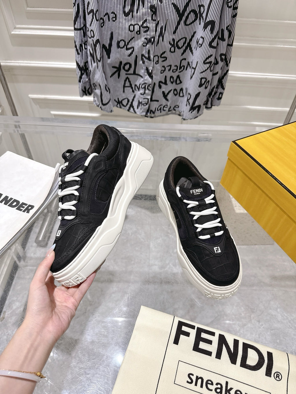 Black Fendi unisex sneakers with white laces and chunky sole, hand-held side view