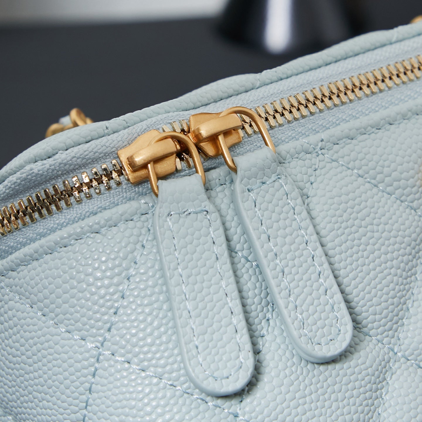 Chanel pebbled leather bag detail, light blue, with gold zipper and braided pull.