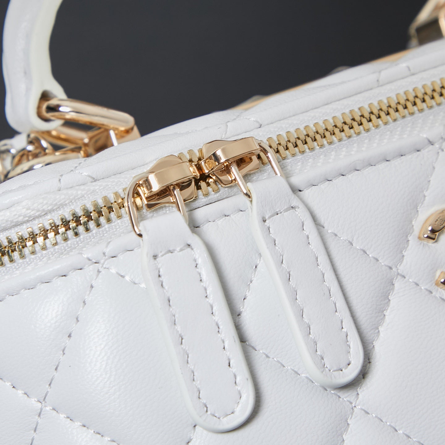 Gold zipper hardware and leather trim on white quilted bag