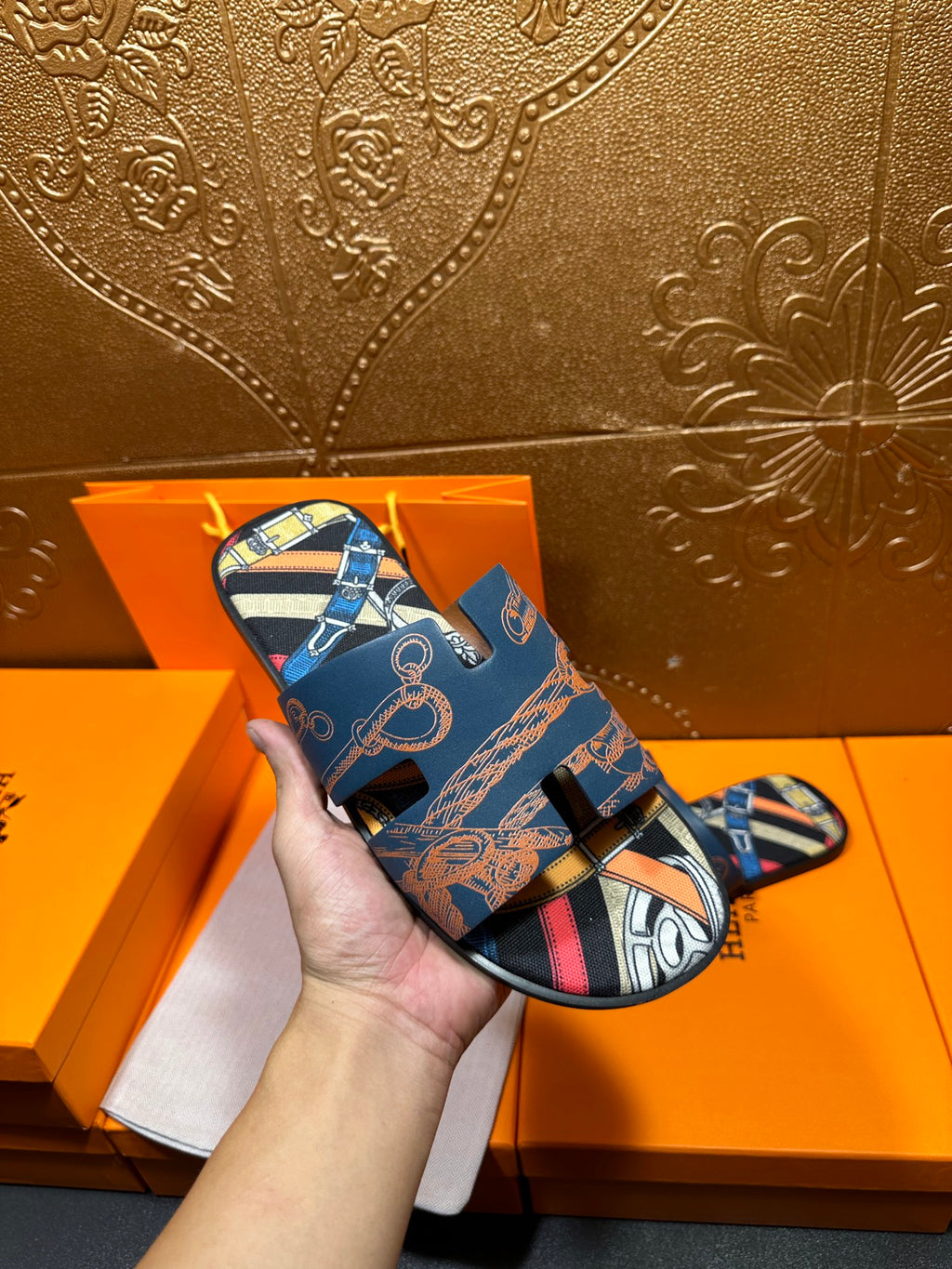 Blue Hermes logo slide sandal held in hand, open toe and patterned strap detail.