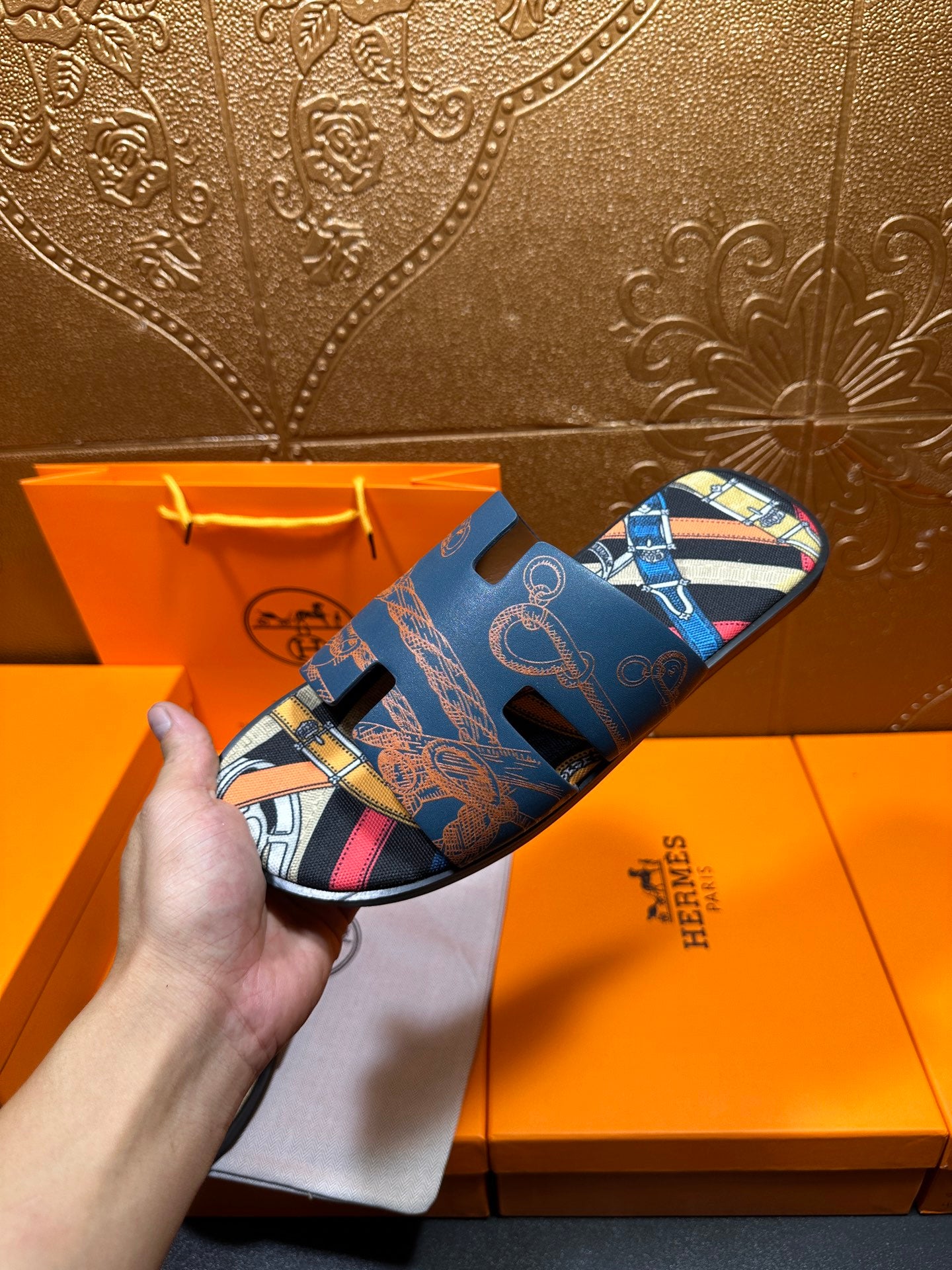 Single blue Hermes logo slide sandal held up, open toe with patterned strap.