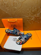 Blue Hermes logo slide sandals with patterned straps and open toe, side-by-side.