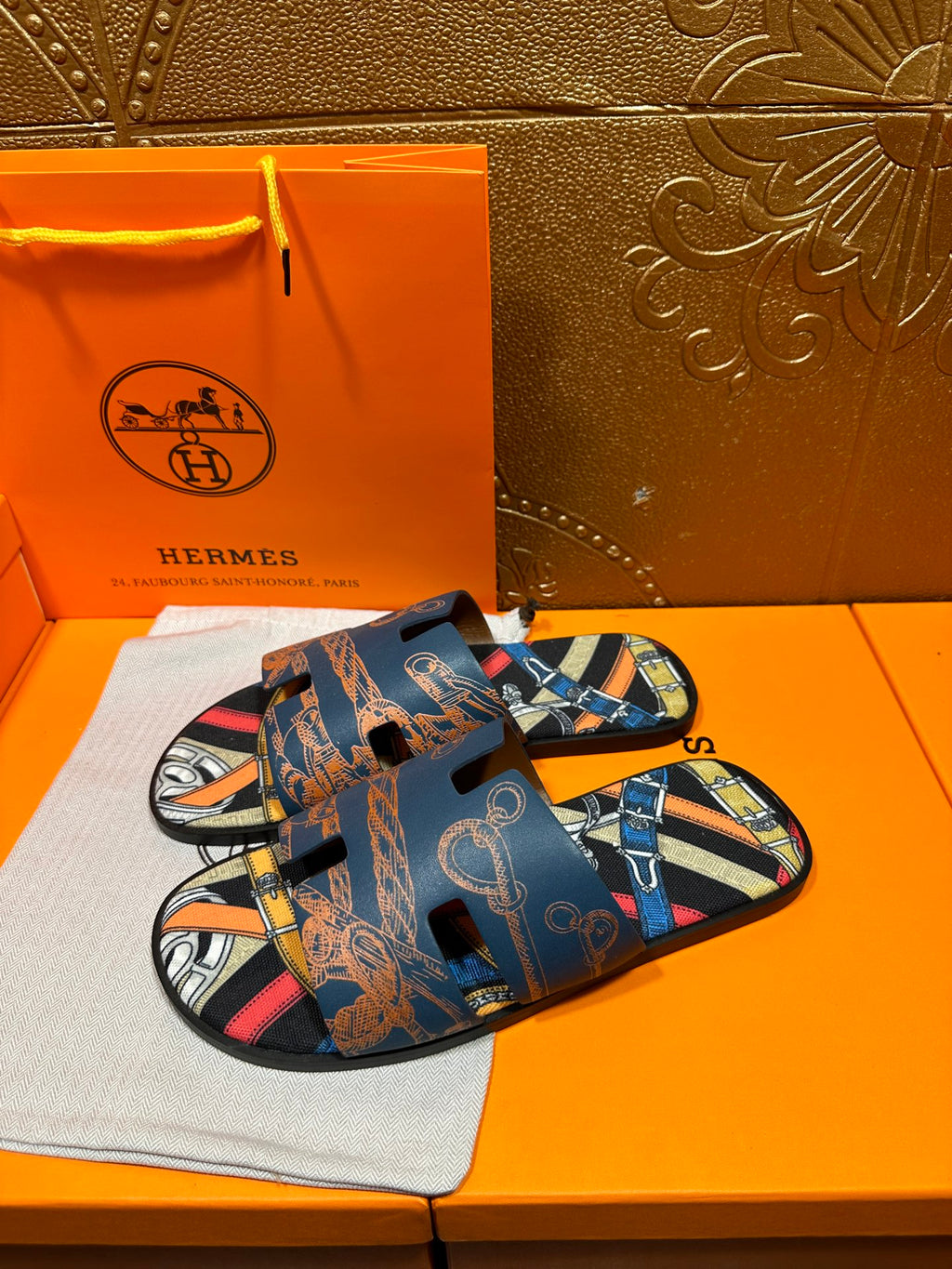 Blue Hermes logo slide sandals with patterned straps and open toe, angled view.